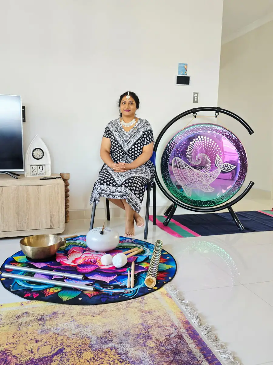 Vinodha seated beside the Whale Song Gong, with singing bowls, a tongue drum, chimes and tuned rods laid out on a lotus mat.