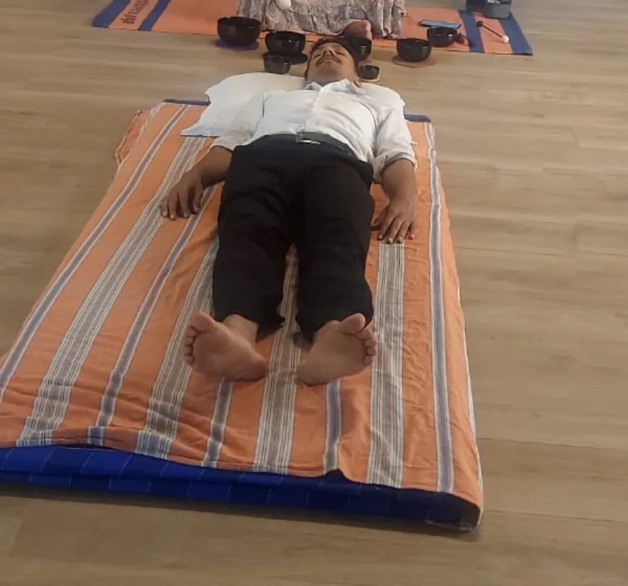 A person resting on a mat with singing bowls placed by their head during a sound bath session.