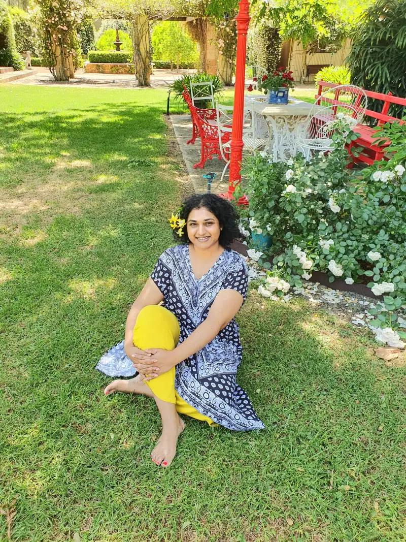 Vinodha sitting on the grass in a rose garden.