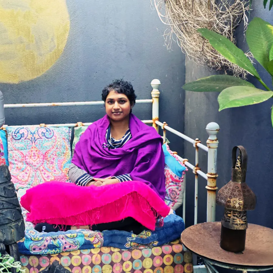Vinodha wrapped in a purple shawl, seated on a daybed.